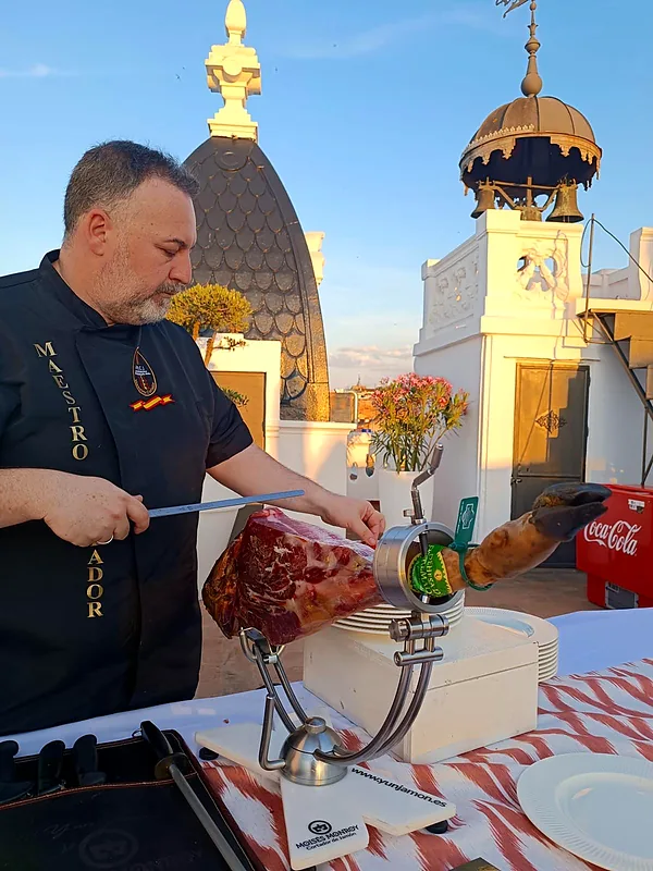 Moisés Monroy cortando jamón en una terraza al atardecer